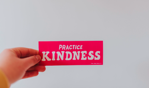 a hand holding a post written practice kindness